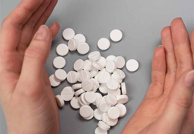 Two hands cradling a pile of white round pills on a table